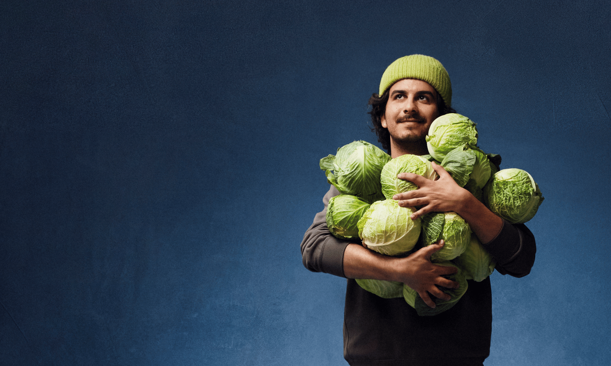 A man holds a huge armful of cabbages. We're talking at least a dozen.