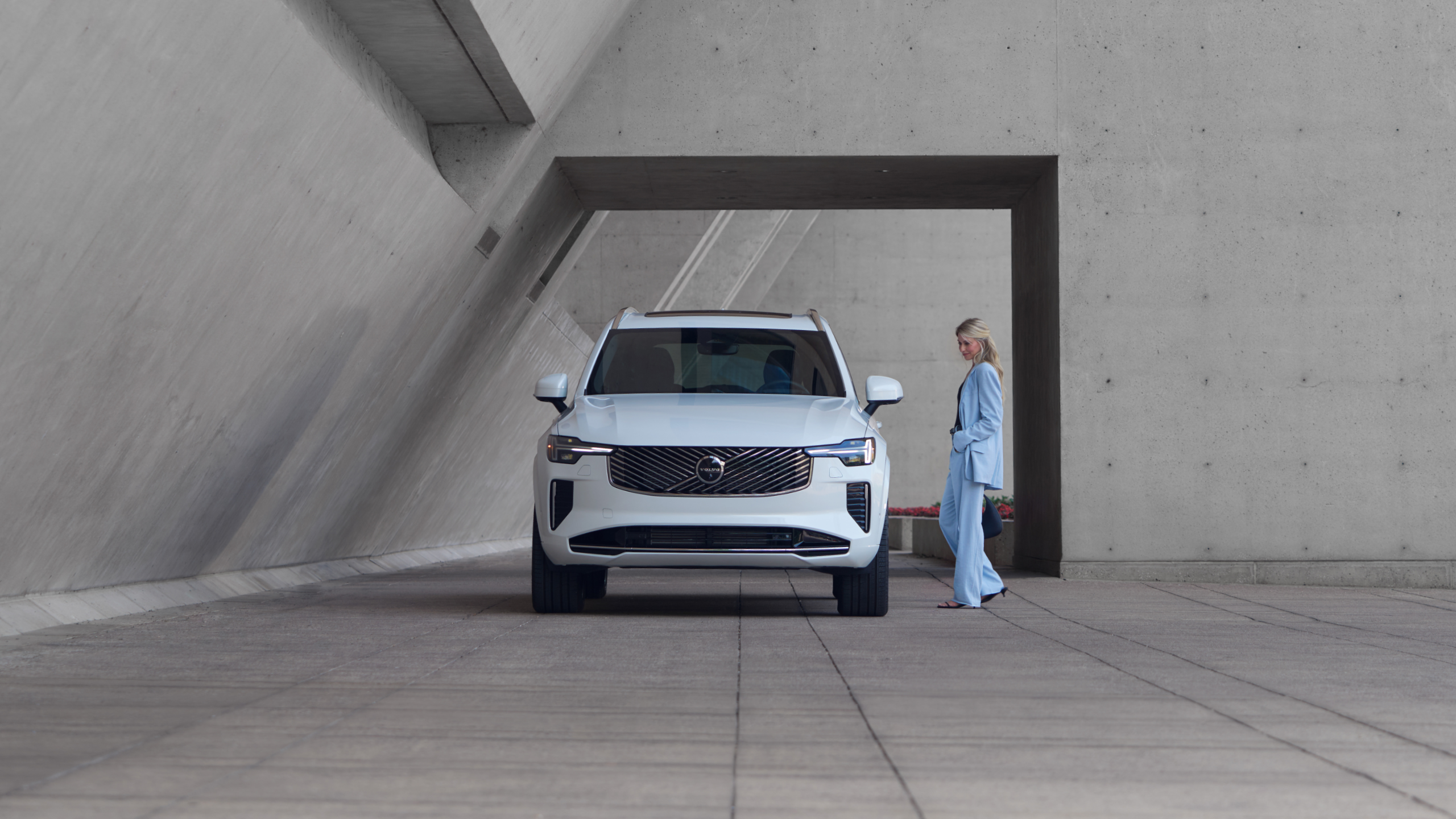 The Volvo XC90 Plug-in hybrid, parked on the side of the road in front of an ocean. A man and woman are unpacking their bags.