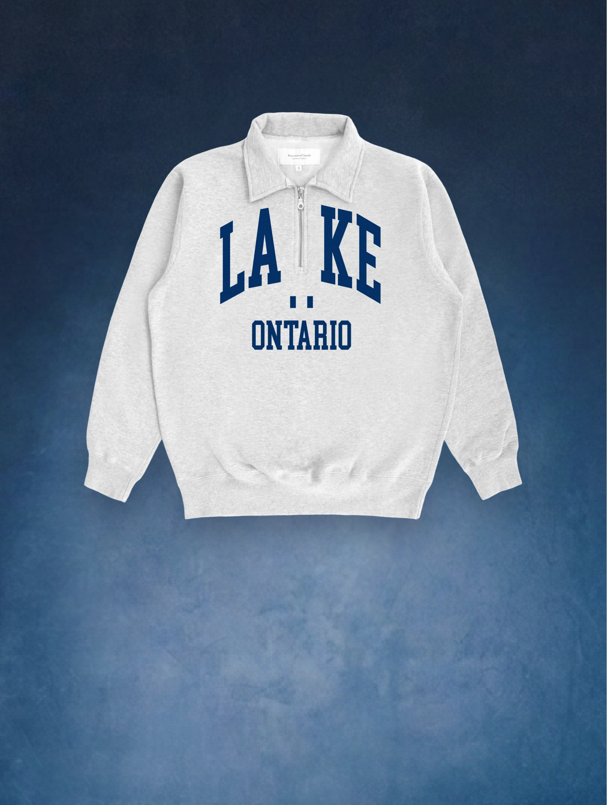 Un chandail Province of Canada. Il est blanc, avec un col, et porte l’inscription « Lake Ontario » en grosses lettres bleues. Il a fière allure!